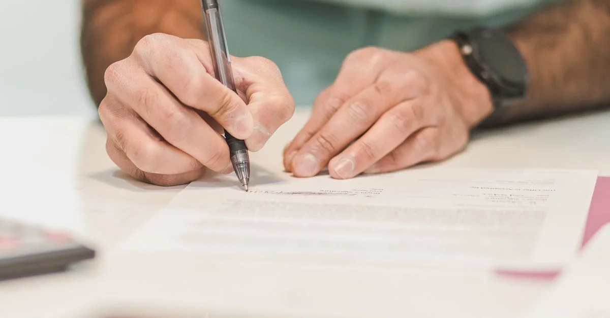 Gros plan sur un homme signant un document officiel avec un stylo à bille sur un bureau.