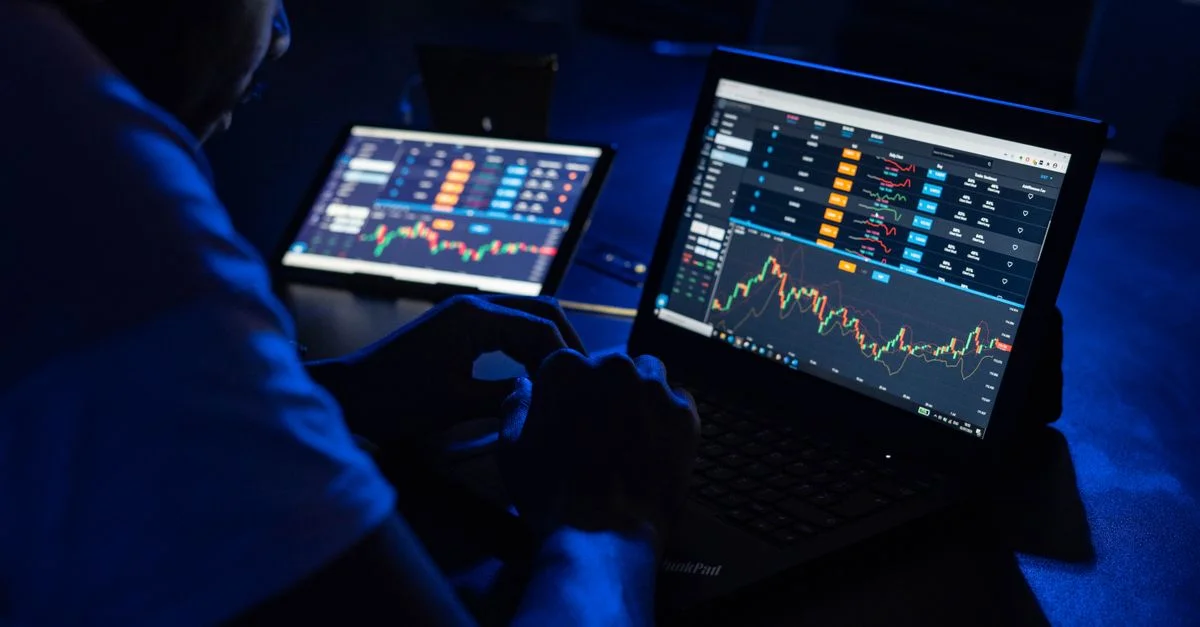 Homme analysant des graphiques et des données financières sur des ordinateurs portables dans une pièce faiblement éclairée, mettant en avant le trading forex.