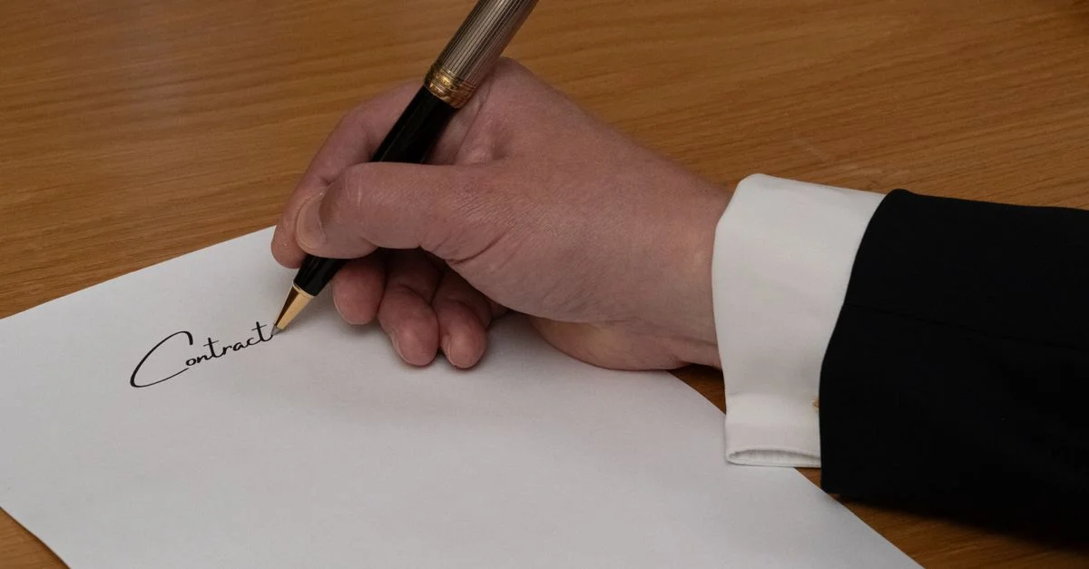 Un professionnel signe un contrat commercial avec un stylo-plume sur un bureau en bois.